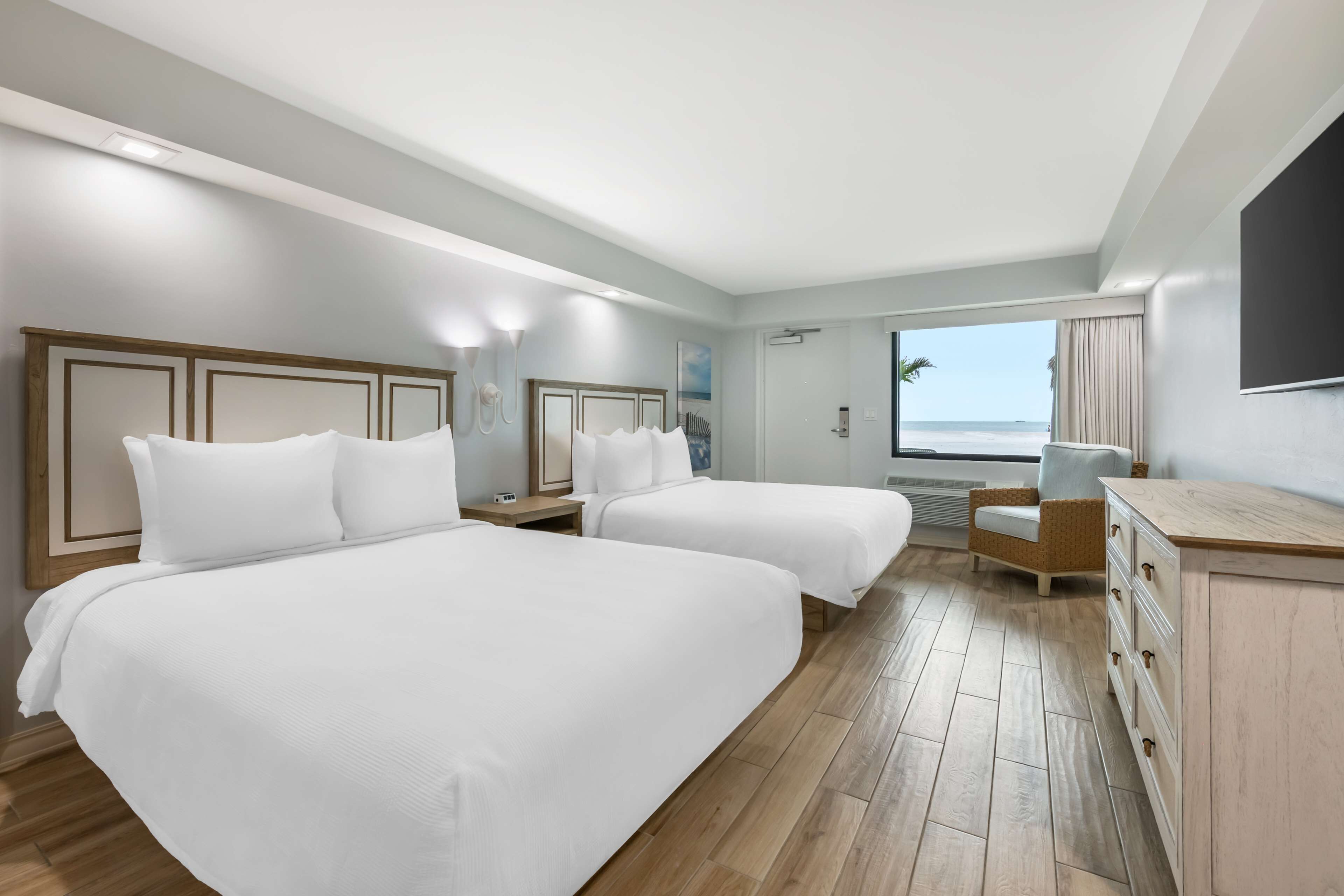 Une chambre d’hôtel avec deux lits, un bureau, une chaise et une vue sur l’océan.