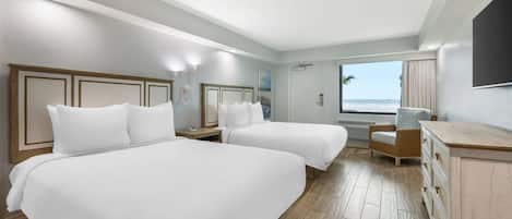 A hotel room with two beds, a desk, a chair, and a view of the ocean.