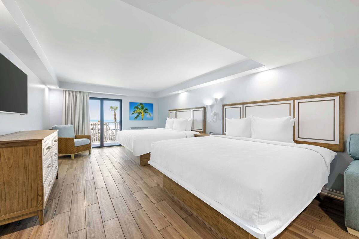 Habitación de hotel con dos camas, un aparador de madera, una silla y un ventanal con vistas.