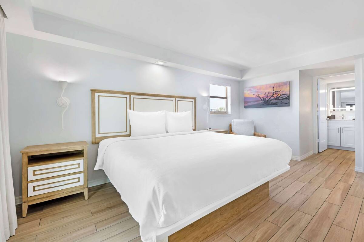 Un dormitorio con una cama grande, una mesita de noche y una lámpara de pared, además de un cuadro.
