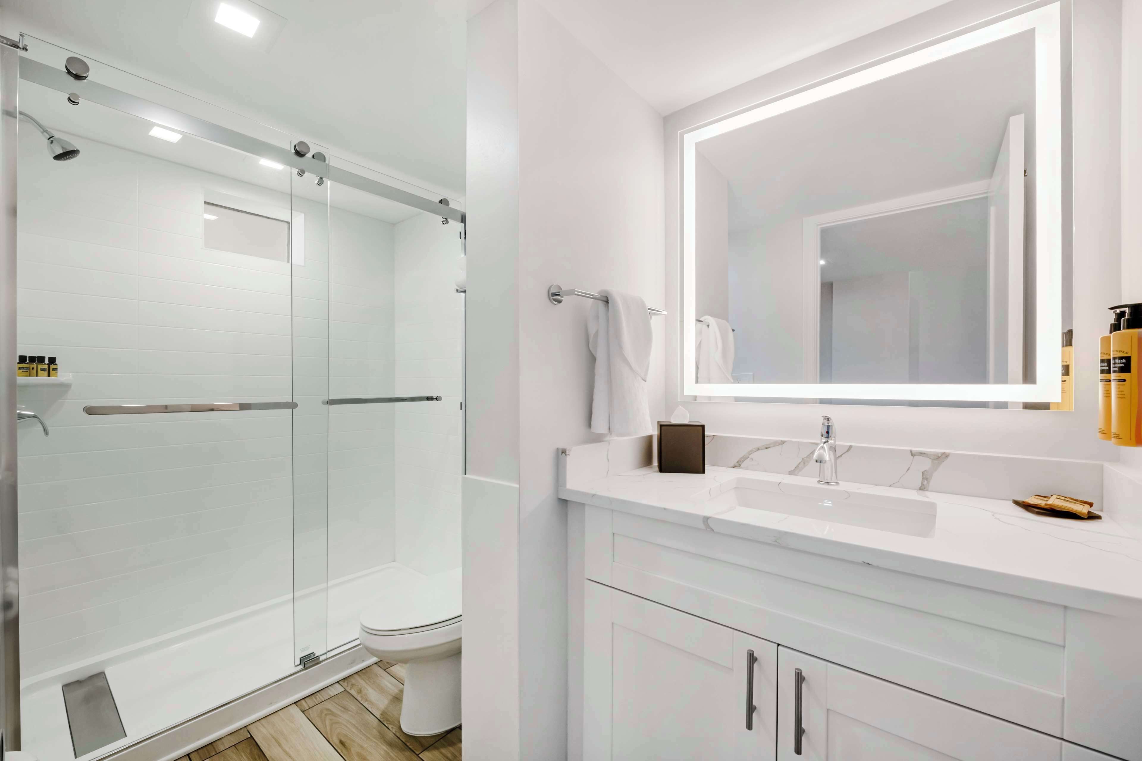 A modern bathroom with a glass-enclosed shower, a white vanity with a large mirror, and a white sink.