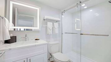A modern bathroom with a white sink, mirror, and toilet. It includes a glass-enclosed shower area with a glass door.