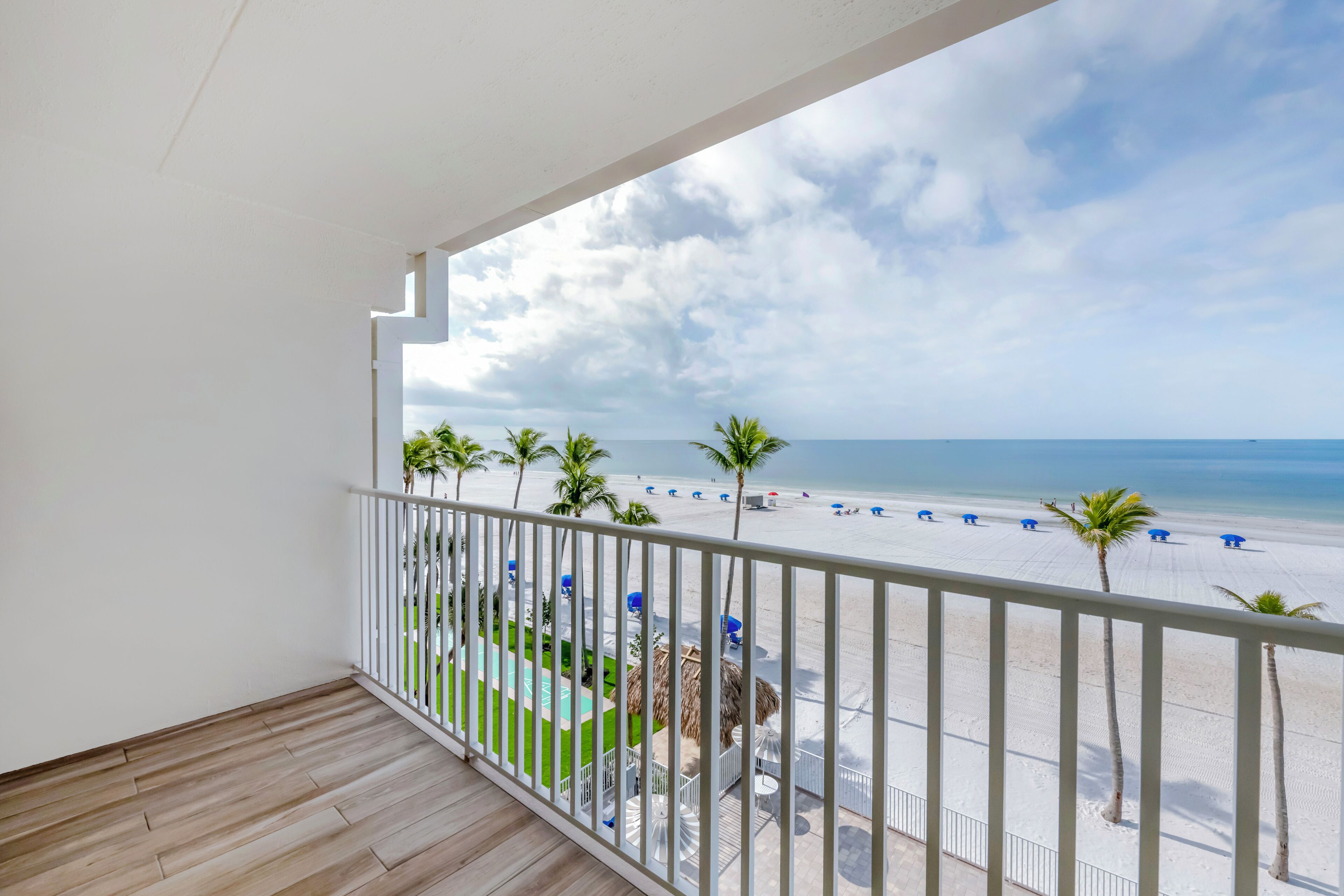 Un balcon avec vue sur une plage, des palmiers et une piscine.