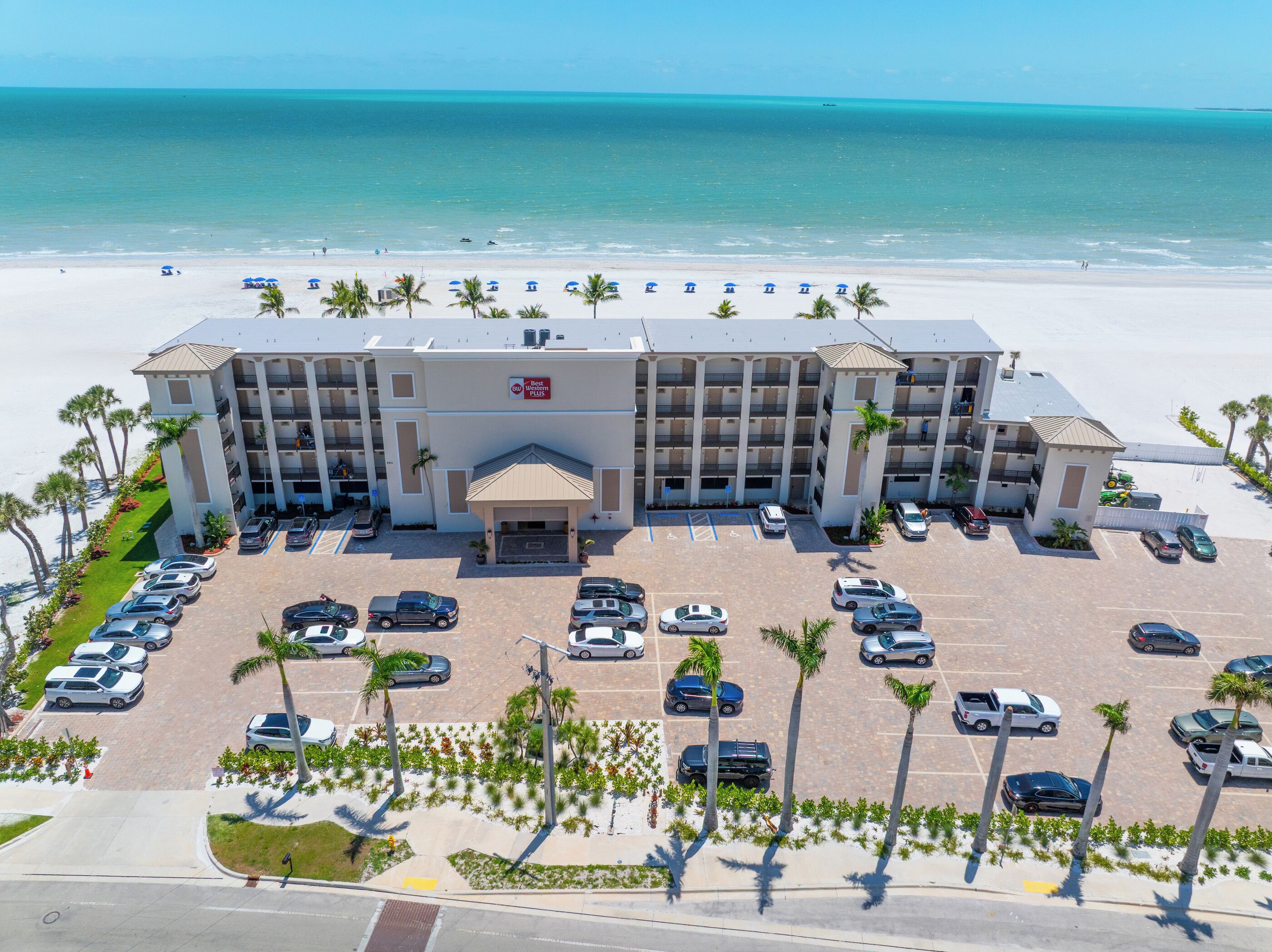A hotel with a parking lot, a beach view, and a sign indicating it is a Best Western Plus.
