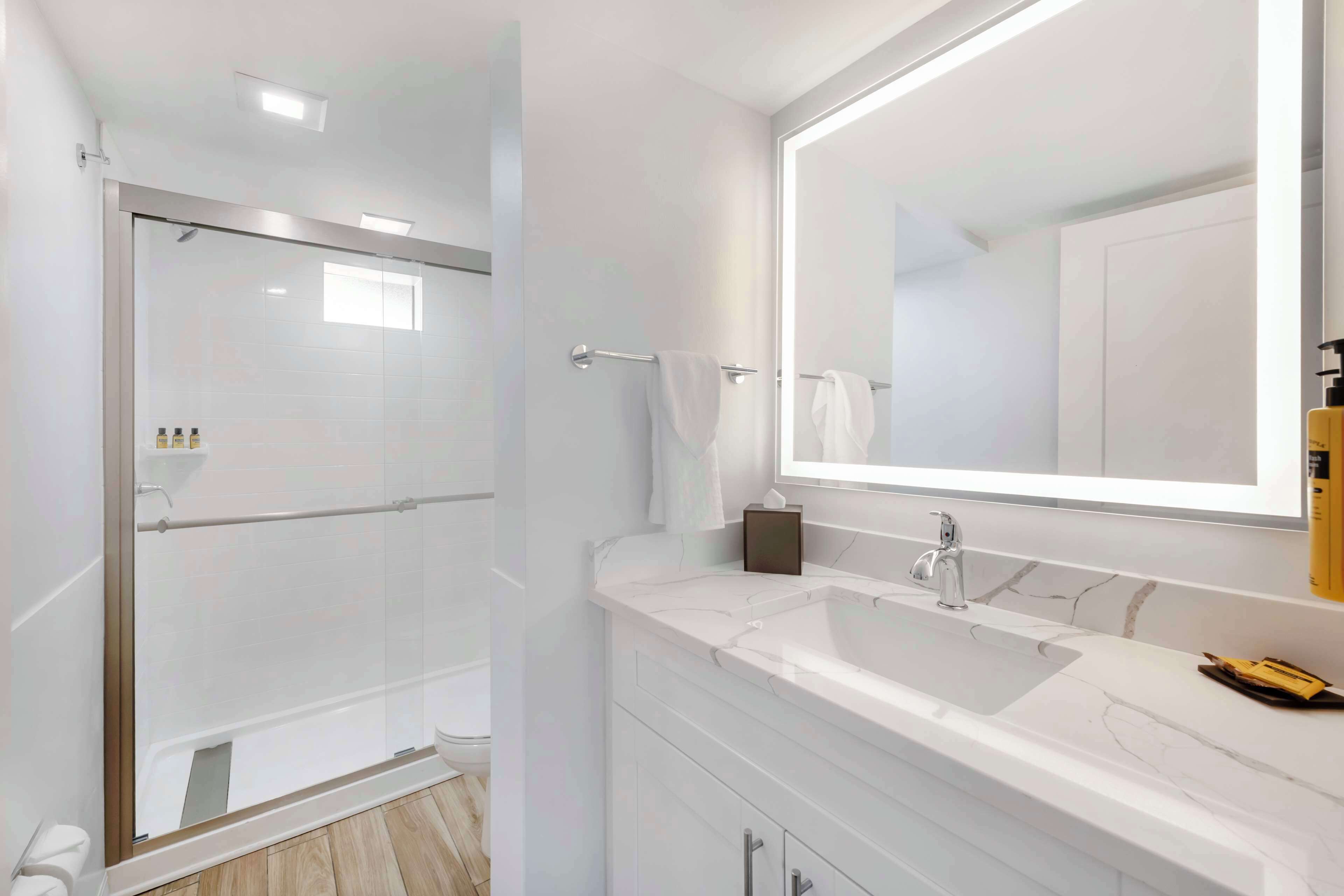 A modern bathroom with a glass-enclosed shower, a large mirror, and a marble sink.