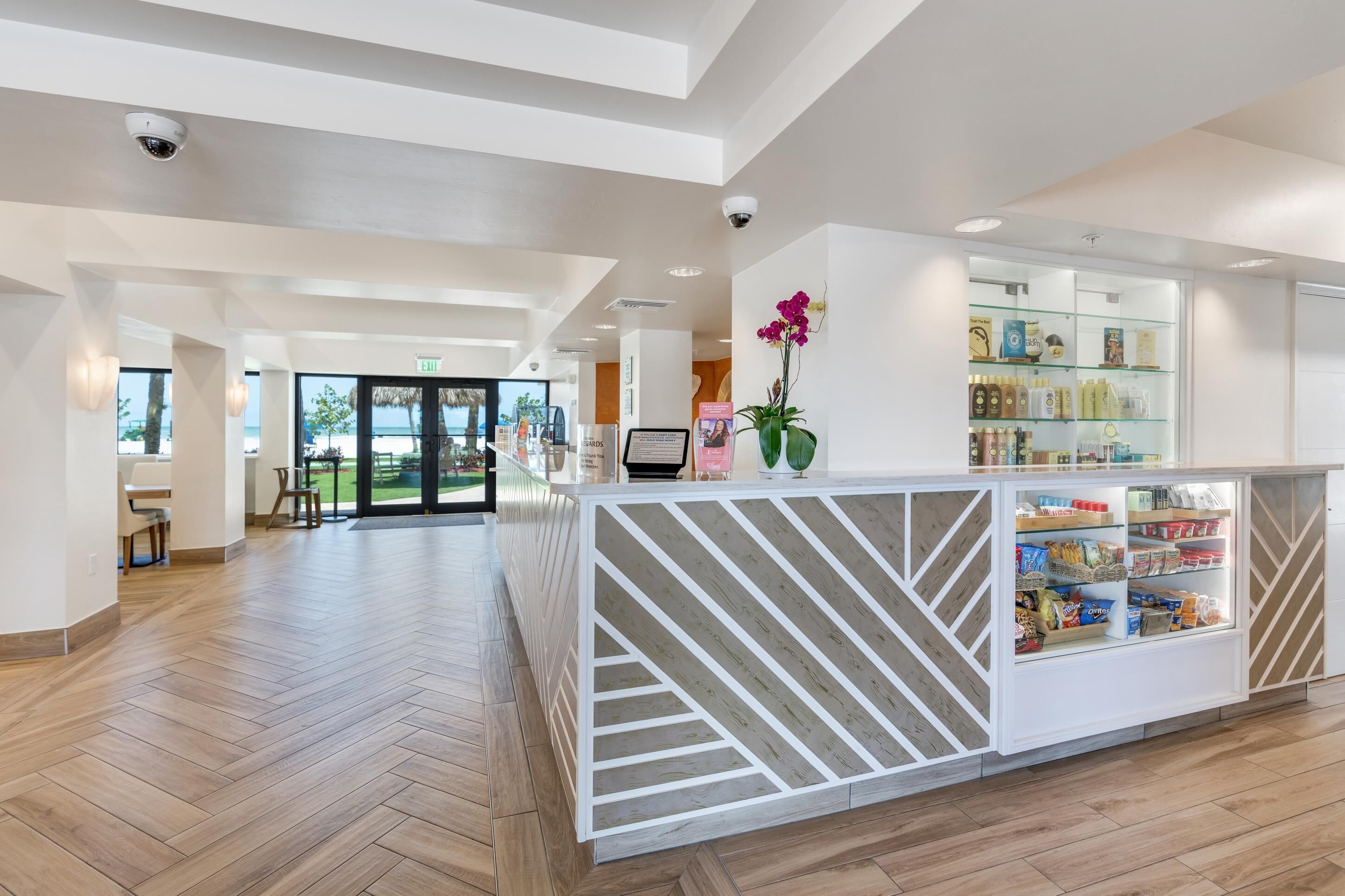 Un área de recepción moderna con un mostrador de patrón espiga, una vitrina con aperitivos y vistas a la playa a través de puertas de cristal.