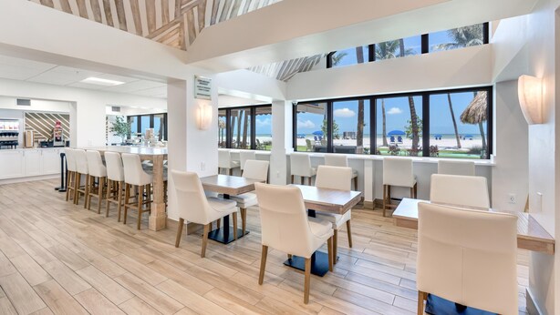 A modern dining area with wooden flooring, white chairs, and large windows offering a view of the beach. - Best Western Plus Beach Resort (Fort Myers Beach)