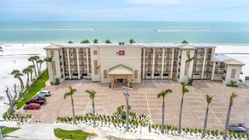 A hotel with a central entrance, multiple parking spaces, and a beach view.
