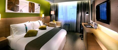 Habitación de hotel con una cama grande, un escritorio, un televisor y una ventana con cortinas.