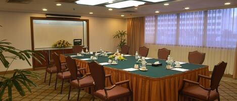 A conference room with a long table, chairs, a projector screen, and a plant.
