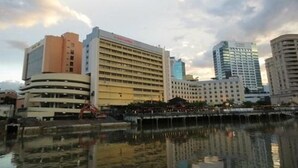 A hotel with multiple floors, a central courtyard, and a body of water reflecting the buildings. - Grand Margherita Hotel (Kuching)