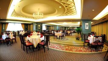 A spacious dining area with round tables and chairs, a patterned carpet, and a chandelier.