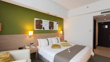 A hotel room with a bed, bedside tables, a lamp, a wall art piece, and a door.