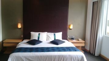 Een hotelkamer met een groot bed, twee nachtkastjes, een wandtelefoon en een raam met gordijnen.