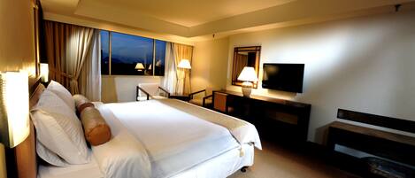 Una habitación de hotel con cama, escritorio, televisor y cortinas.