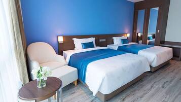Ein Hotelzimmer mit zwei Betten, einem Sessel, einem kleinen Tisch mit einer Vase und einem Spiegel.