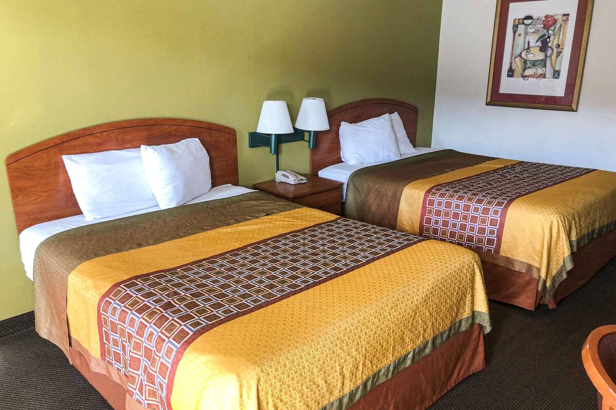 A hotel room with two beds, each with a patterned bedspread, a nightstand with a lamp, and a wall-mounted artwork.