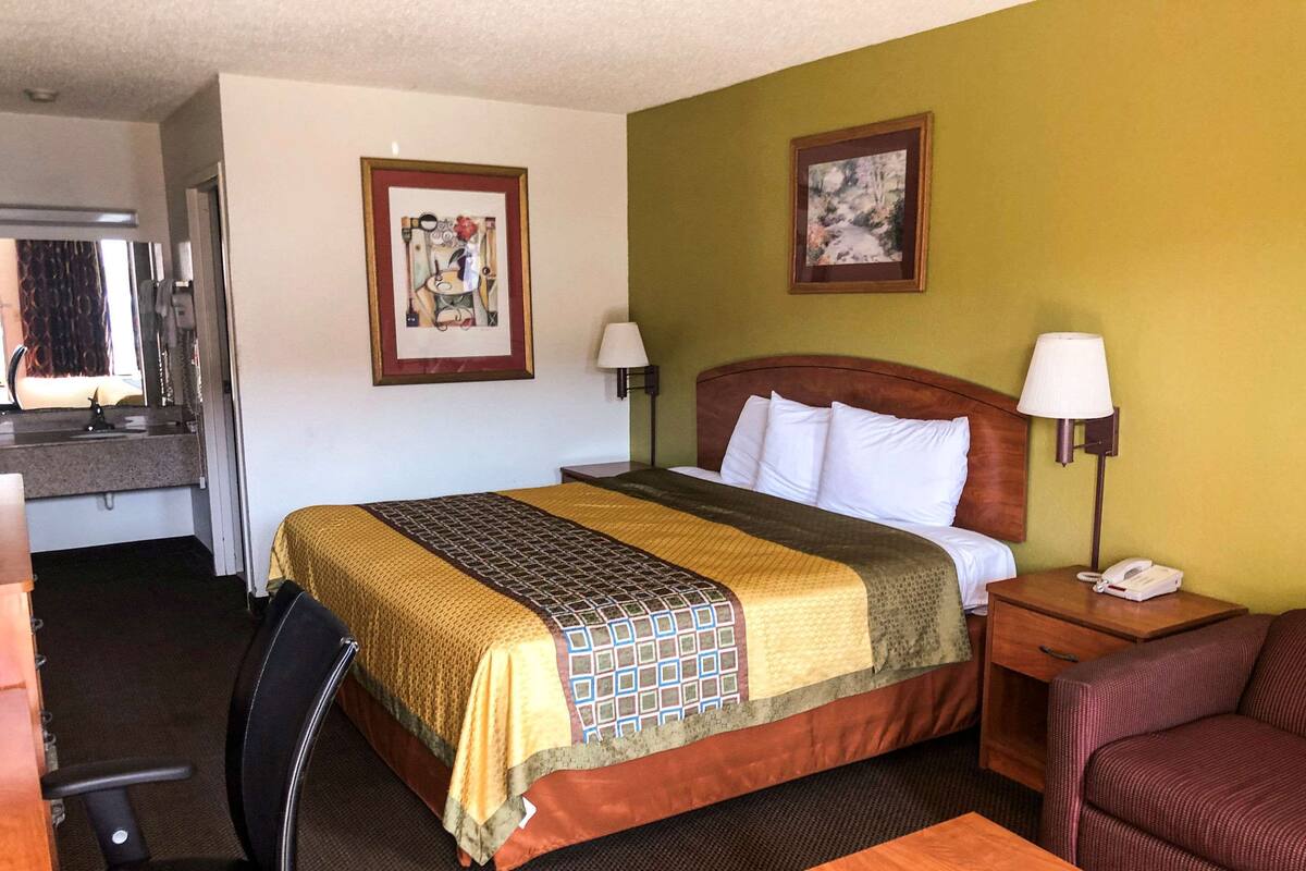 A hotel room with a bed, a desk, a chair, and two paintings on the walls.