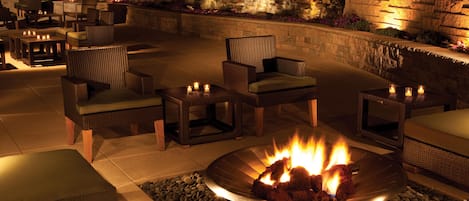 An outdoor patio area with wicker furniture, a stone wall, and a fire pit.