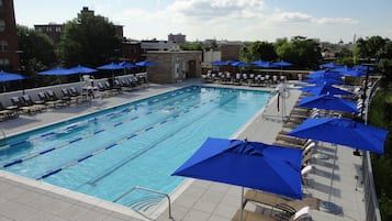Una piscina con diverse corsie, lettini e ombrelloni blu.