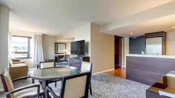 A hotel room with a dining area, a TV, a sofa, and a large window.