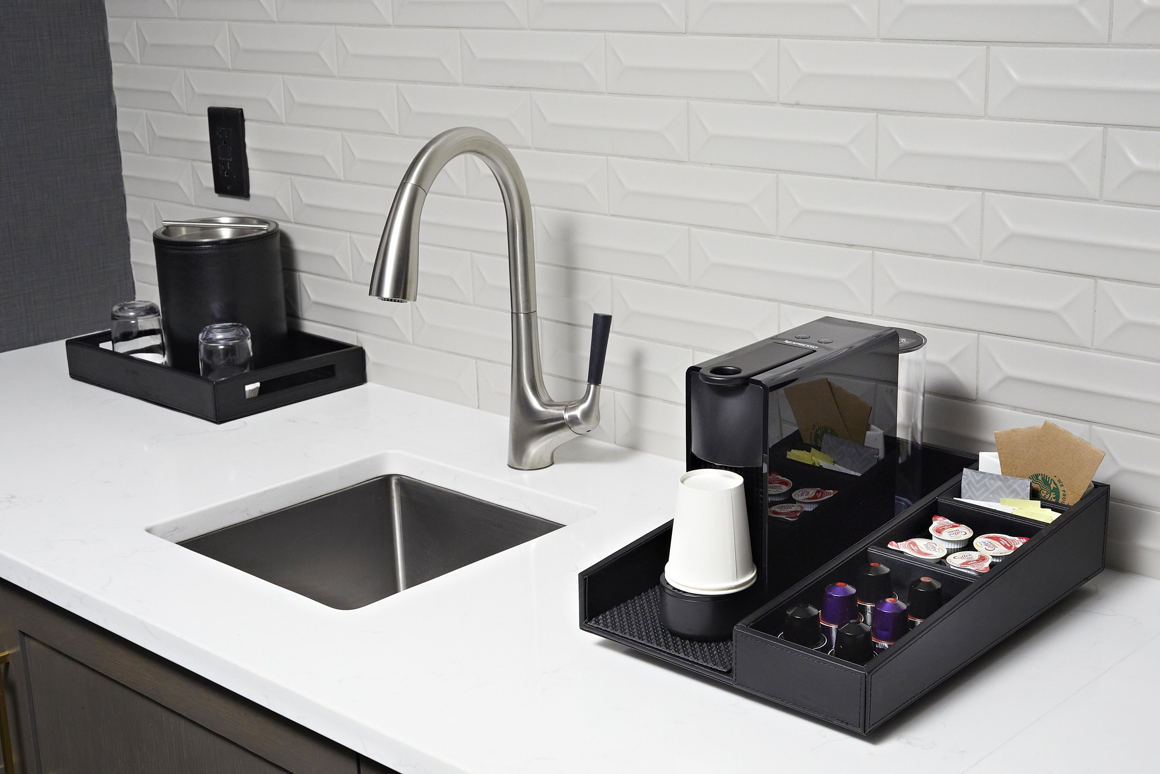 A modern kitchen with a stainless steel faucet, a coffee maker, and a coffee pod dispenser.