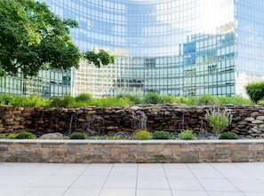 Un edificio moderno con fachada de vidrio, un muro de contención de piedra y una fuente de agua.