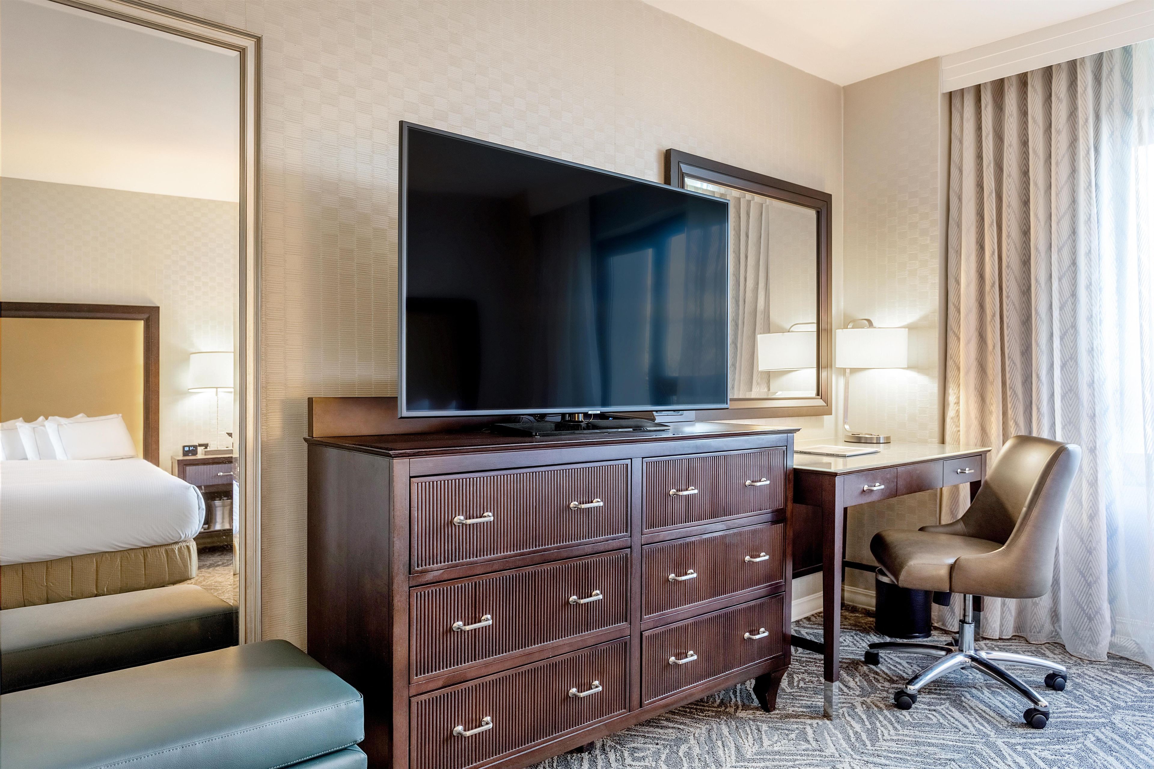Habitación de hotel con cama, escritorio con televisor, silla y cómoda.