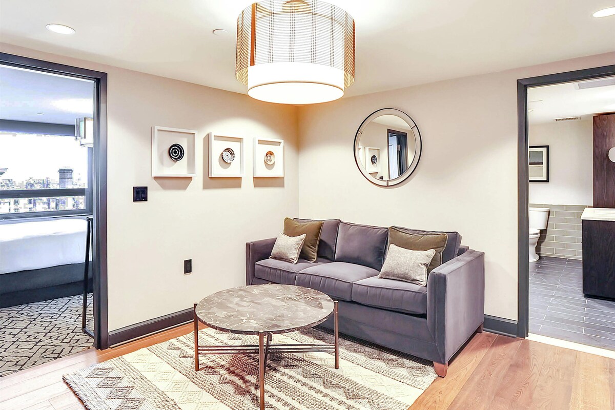 A modern living room with a grey sofa, a round coffee table, and a large window.