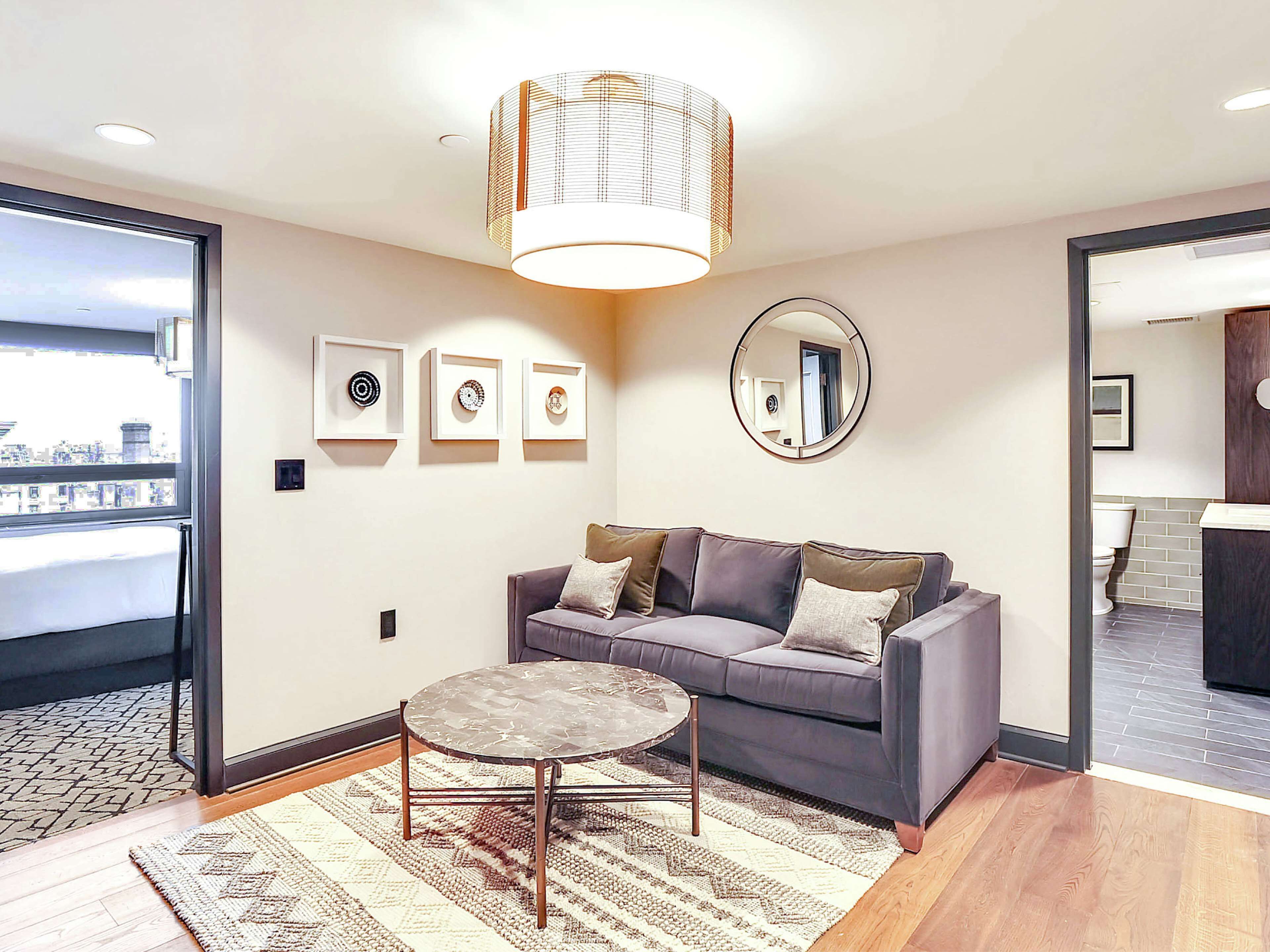A modern living room with a grey sofa, a round coffee table, and a large window.