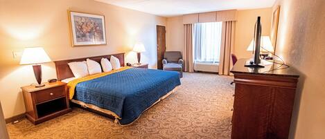 Habitación de hotel con una cama grande, dos mesitas de noche con lámparas, un escritorio con computadora, una silla y una ventana con cortinas.