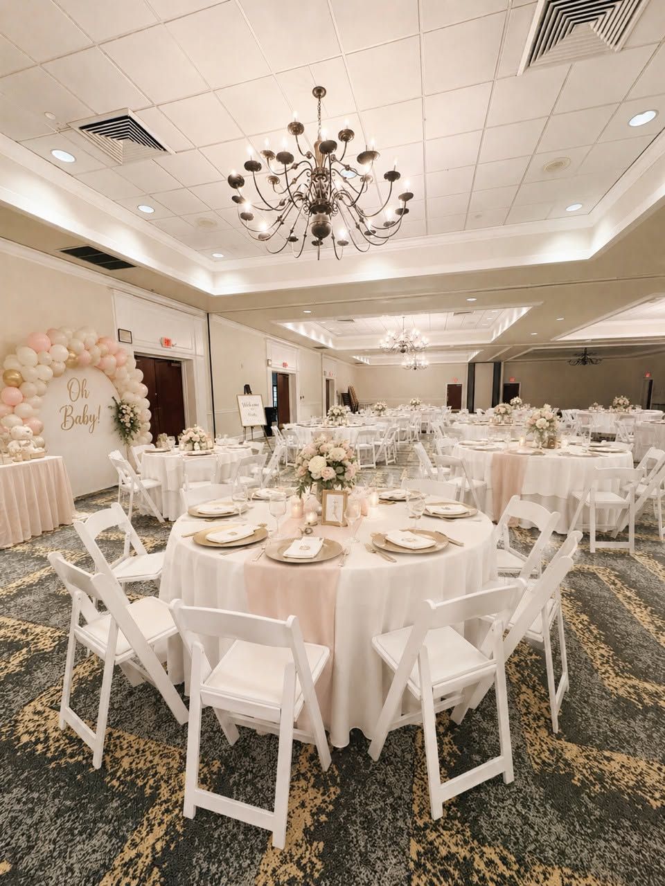 A banquet hall with round tables, white chairs, and a chandelier.