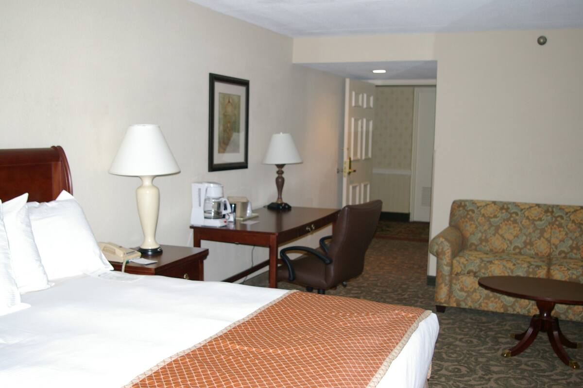 A hotel room with a bed, a desk with a lamp, a chair, a sofa, and a small table.