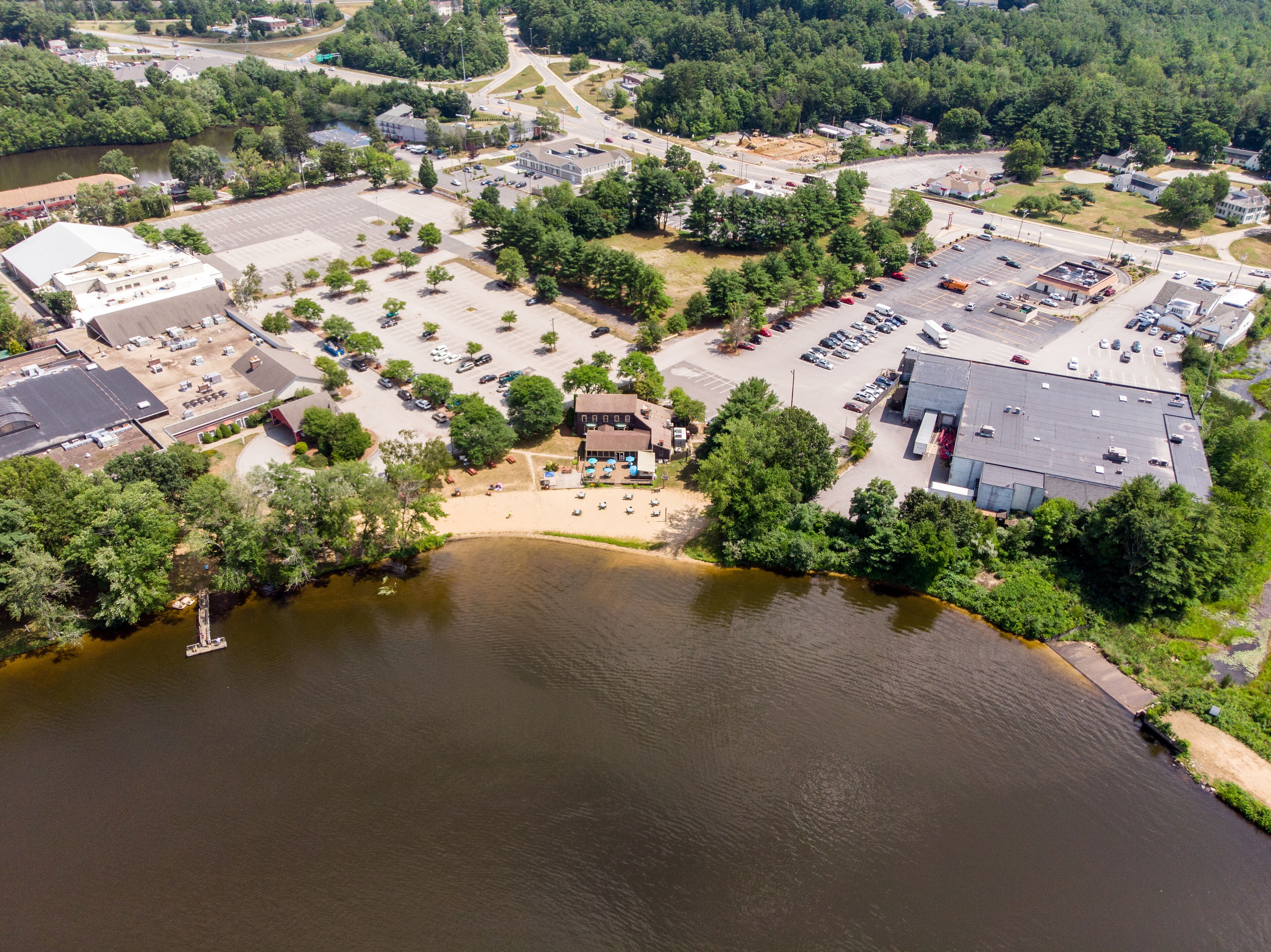 Vue aérienne d’une zone commerciale avec des parkings, des immeubles et une rivière.
