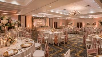 A banquet hall with round tables, chairs, and floral centerpieces.