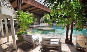 Ein Poolbereich im Innenbereich mit Holzterrasse, Liegestühlen und einer kleinen Insel im Pool.