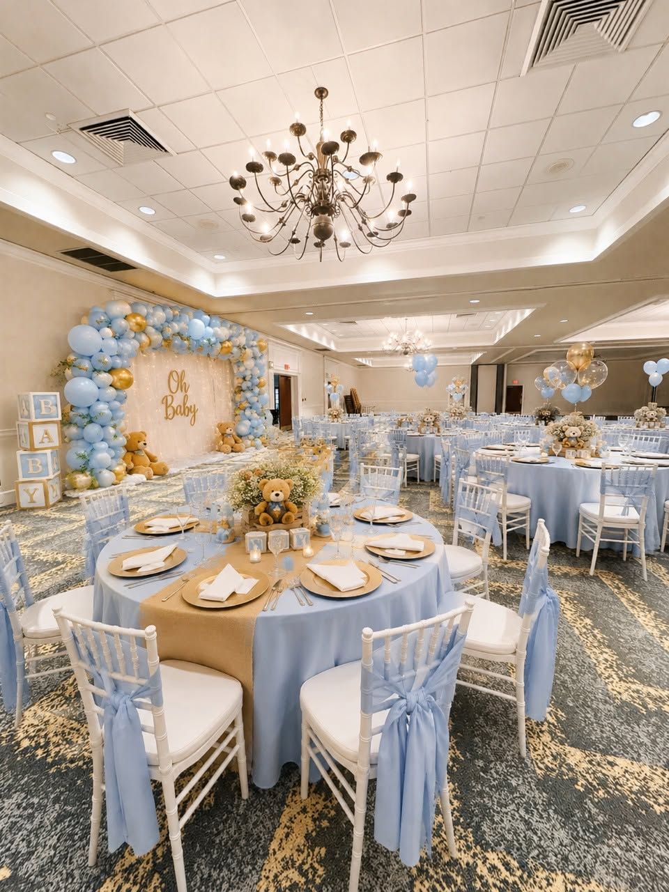 Un salón de banquetes con mesas redondas, sillas y un escenario central con un letrero que dice 'Baby'.