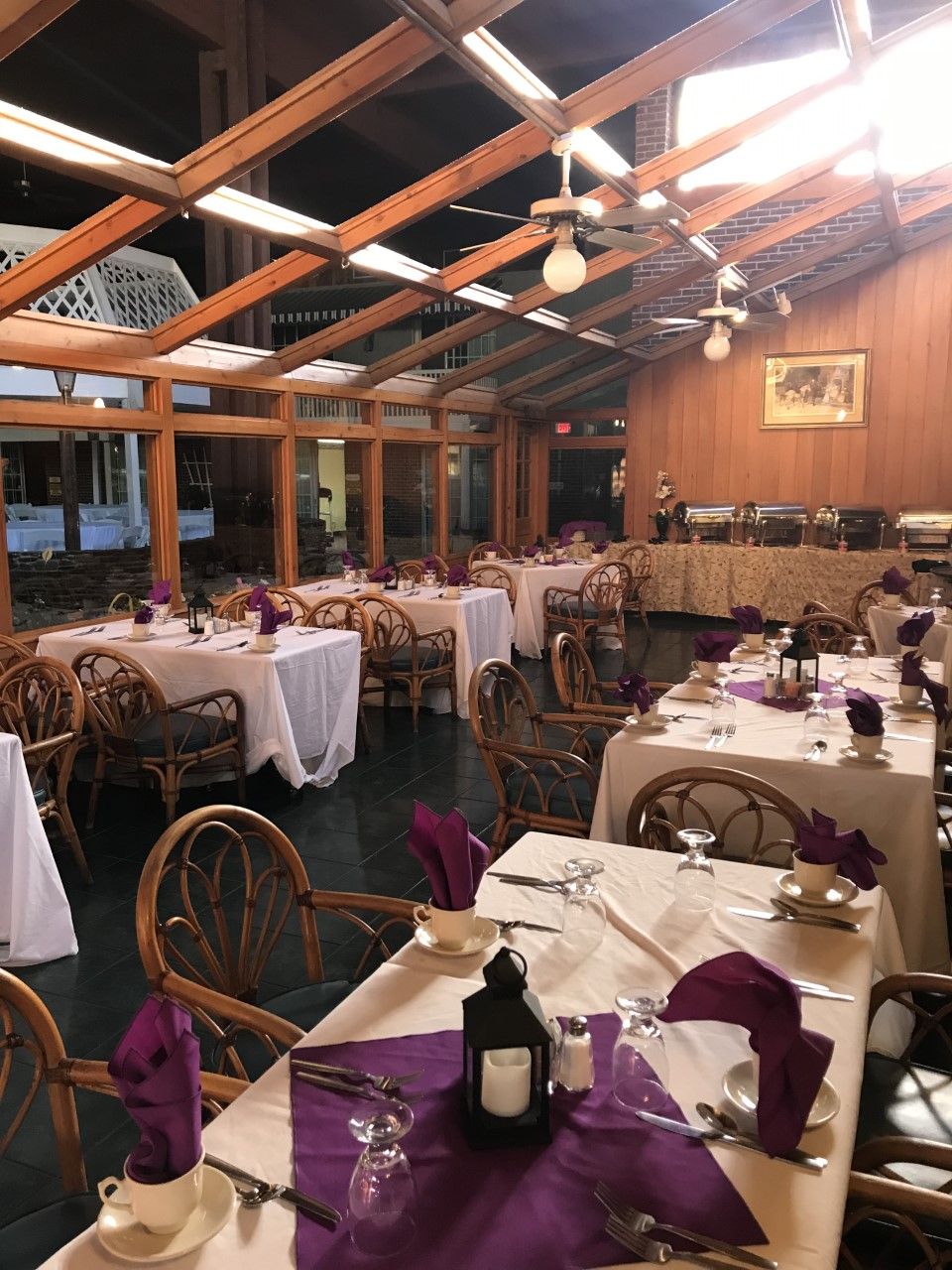 Un restaurante con varias mesas dispuestas para comer, sillas de madera y un techo alto con vigas a la vista.