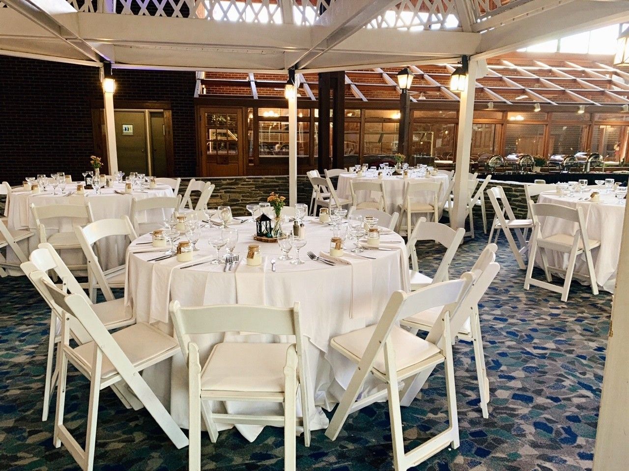 A banquet hall with round tables set for dining, white chairs, and a patterned carpet.