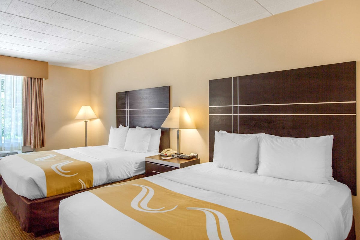 A hotel room with two beds, each with a headboard, bedside lamps, and a large window with curtains.