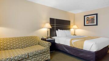 A hotel room with a bed, two bedside lamps, a patterned sofa, and a framed picture on the wall.