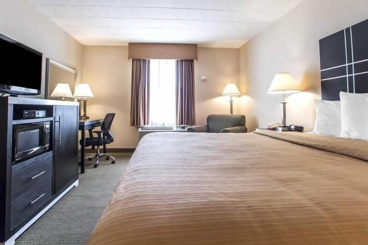 A hotel room with a bed, desk, chair, television, and lamps.