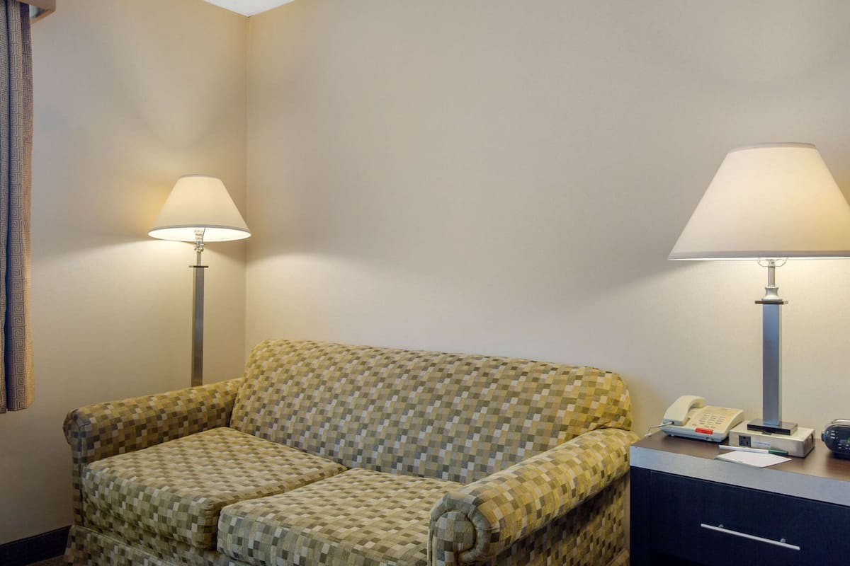A hotel room with a checkered armchair, two bedside lamps, a desk with a telephone, and a small drawer.