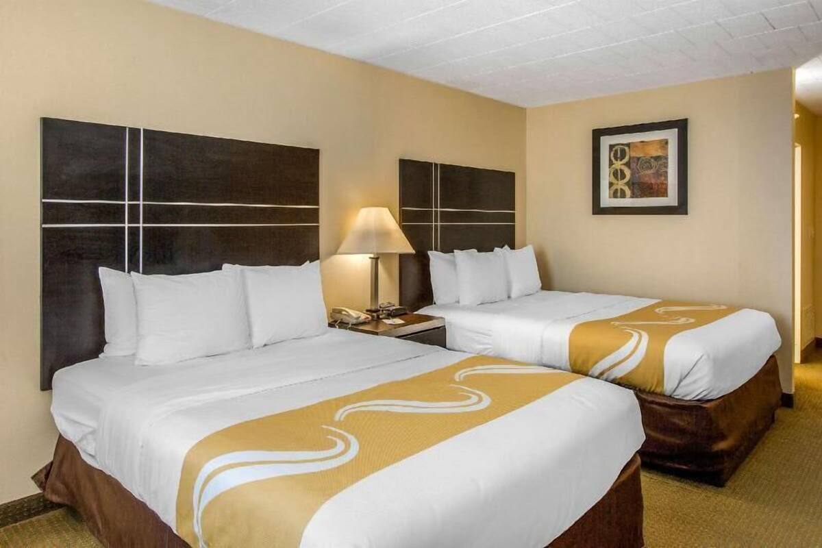 A hotel room with two beds, a nightstand, a lamp, and a framed picture on the wall.