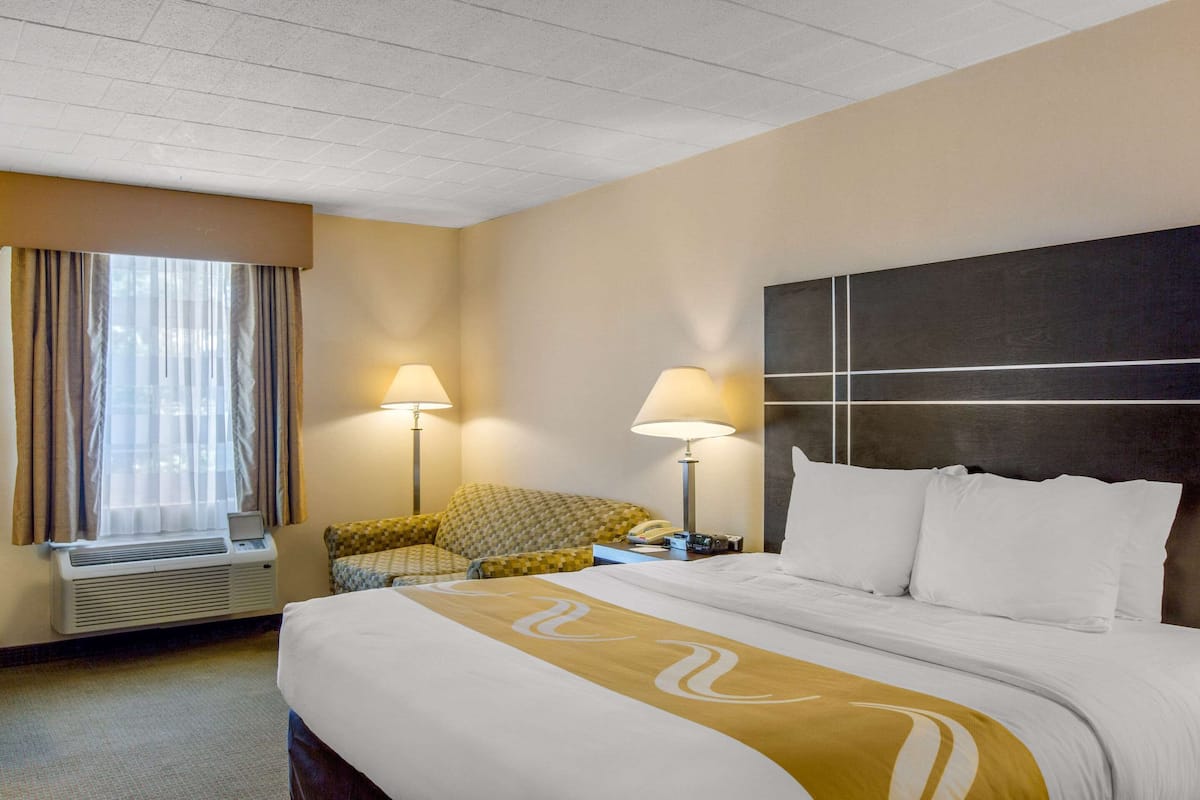A hotel room with a large bed, two bedside lamps, a chair, and a window with curtains.