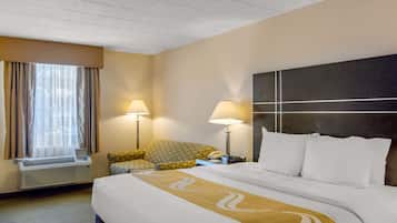 Quarto de hotel com uma cama grande, duas luminárias de cabeceira, uma cadeira e uma janela com cortinas.