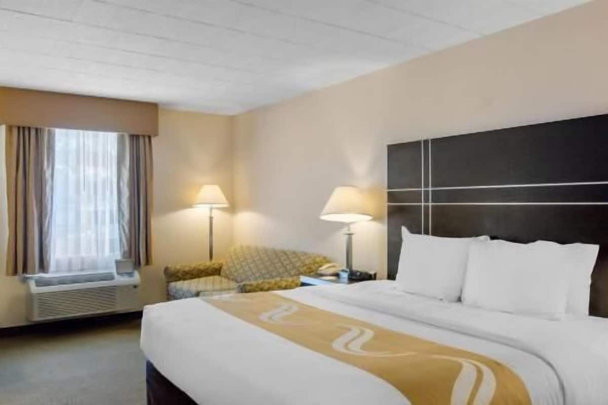 A hotel room with a bed, two bedside lamps, a chair, and a window with curtains.