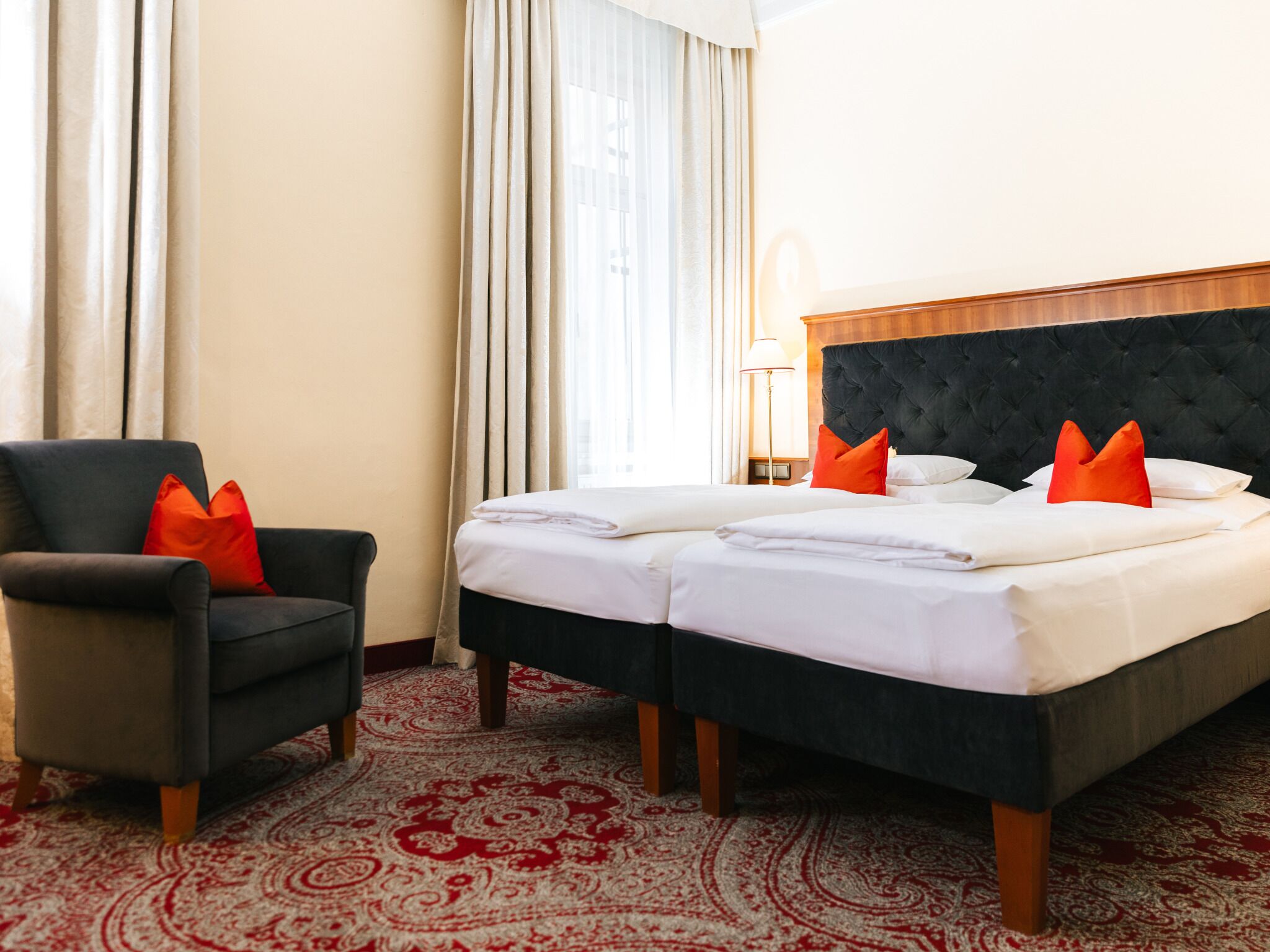 A hotel room with a bed, two pillows, a chair, a lamp, and a patterned carpet.