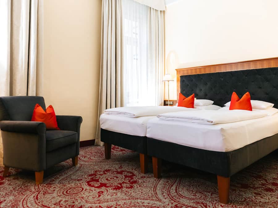 A hotel room with a bed, two pillows, a chair, a lamp, and a patterned carpet.