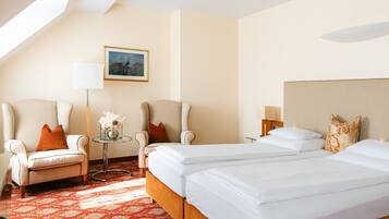 A hotel room with two beds, a sofa, a small table with a vase of flowers, a lamp, and a painting on the wall.